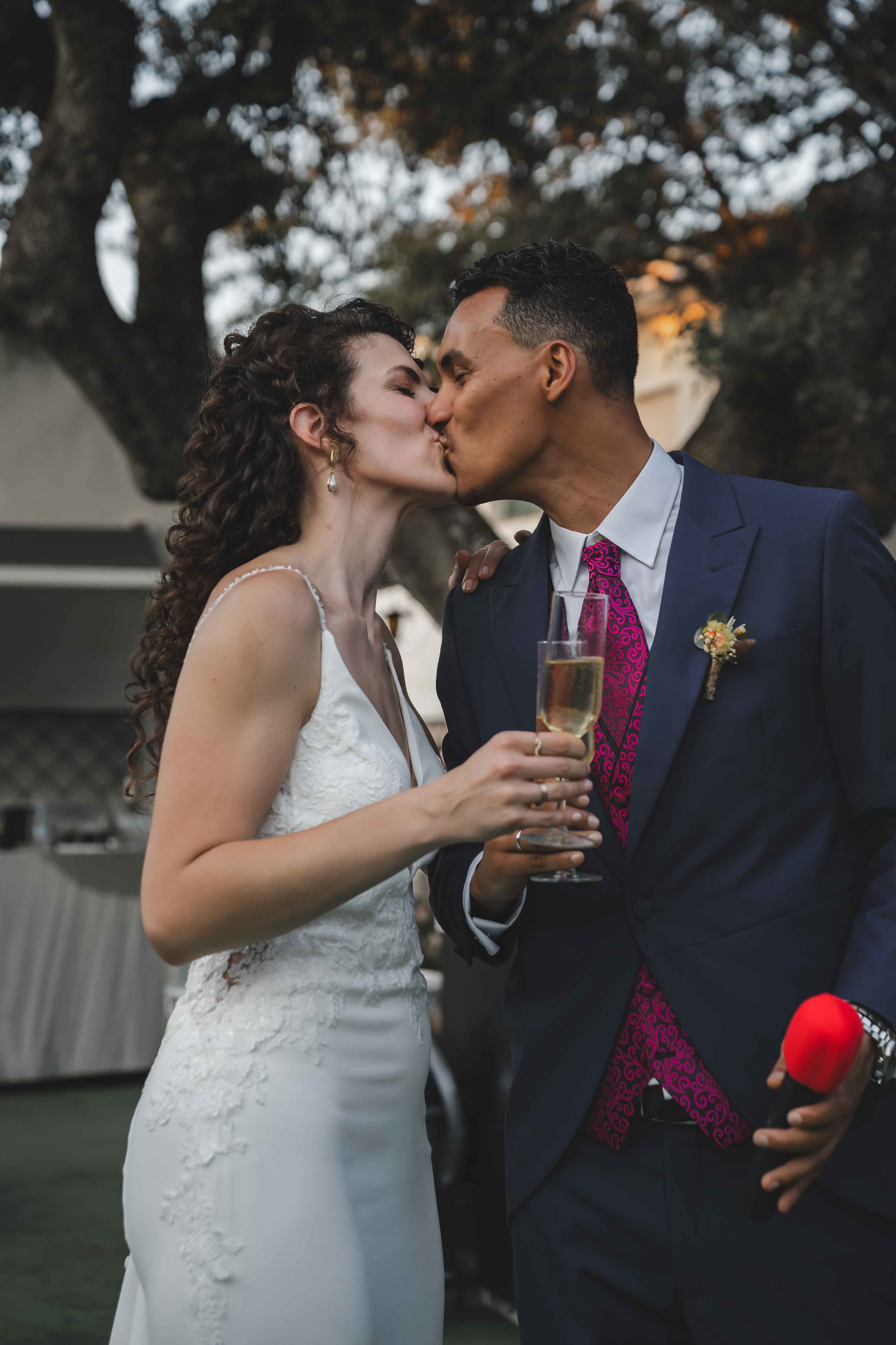 Maria and Leo kissing with champagne glasses in hand during the outdoor reception