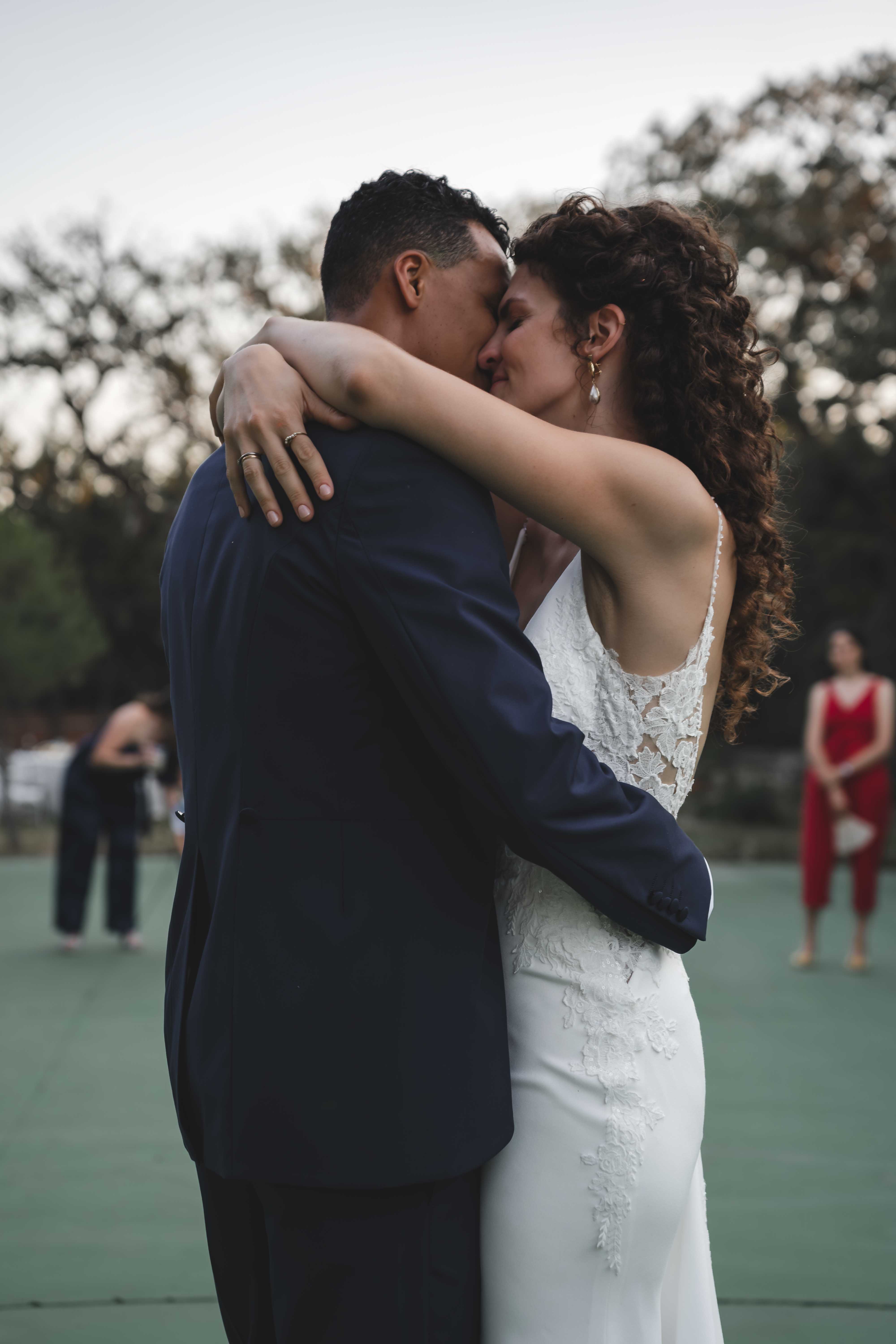 Maria and Leo sharing a kiss during their outdoor first dance at sunset, guests in the background
