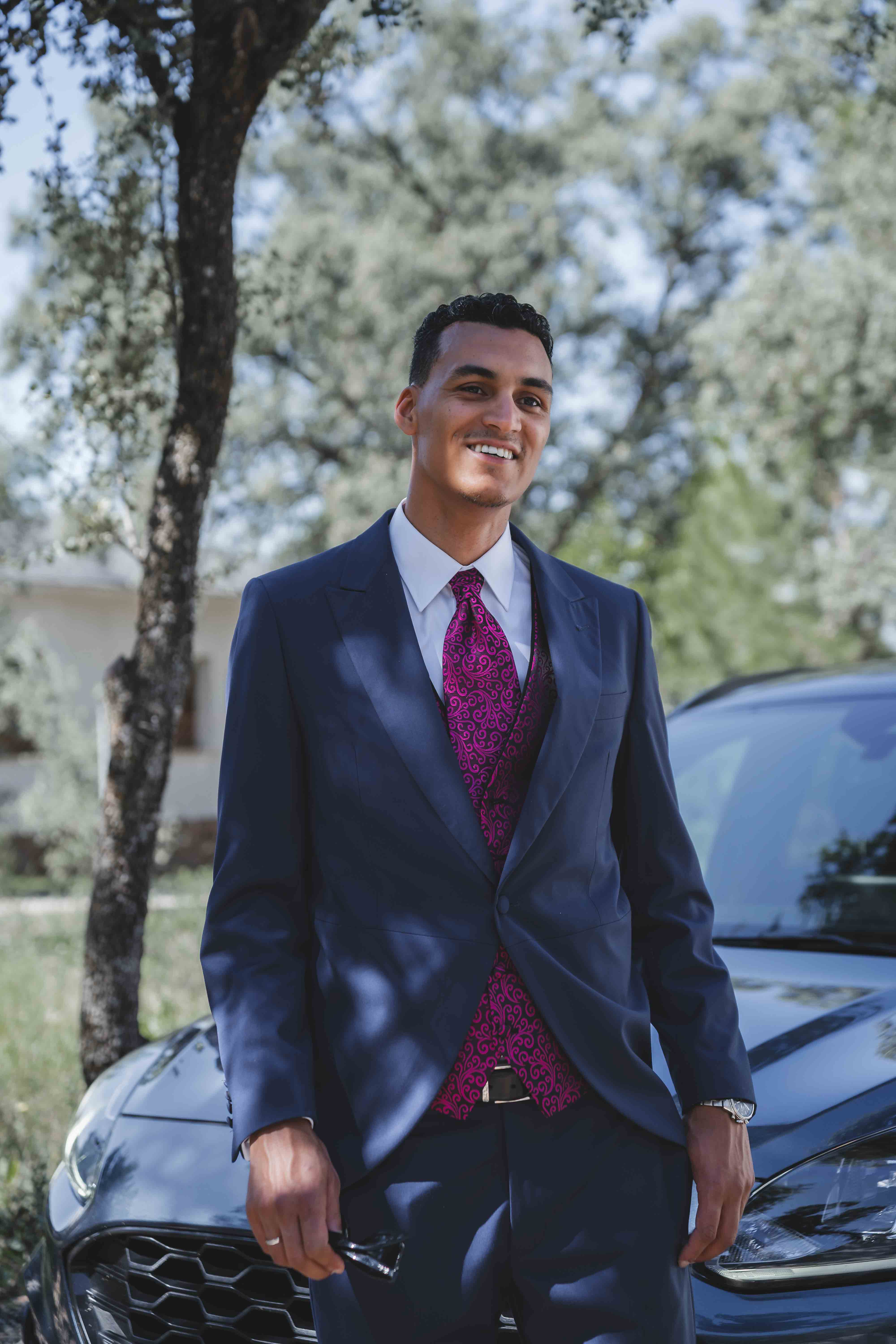Leo smiling in his navy suit with patterned burgundy tie, standing by the car before the ceremony