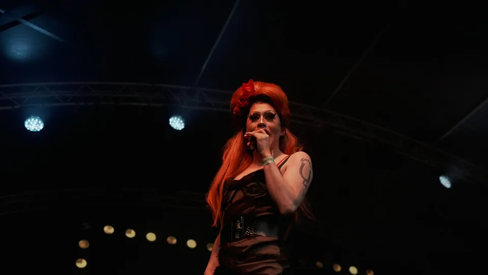 Northern Pride performer singing into a microphone beneath stage lights
